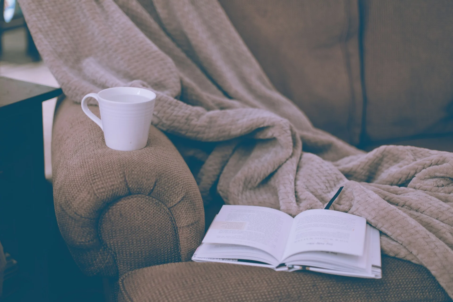 A cozy armchair with a warm blanket, an open book, and a mug of coffee